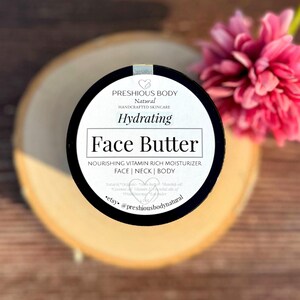 May include: A glass jar with a black lid filled with a face butter. The jar has a white label with the text 'PRESHIOUS BODY', 'Natural', 'HANDCRAFTED SKINCARE', 'Hydrating', 'Face Butter', 'NOURISHING VITAMIN RICH MOISTURIZER', 'FACE | NECK | BODY', 'Natural Organic Shea butter Rosehip oil Coconut Vitamin E Essential oils of Frankincense Lybguder', 'etsy. @preshiousbodynatural'.