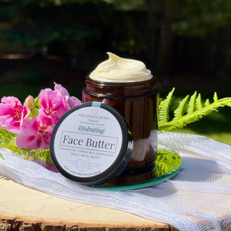 May include: A glass jar with a black lid filled with a face butter. The jar has a white label with the text 'PRESHIOUS BODY', 'Natural', 'HANDCRAFTED SKINCARE', 'Hydrating', 'Face Butter', 'NOURISHING VITAMIN RICH MOISTURIZER', 'FACE | NECK | BODY', 'Natural Organic Shea butter Rosehip oil Coconut Vitamin E Essential oils of Frankincense Lavender', 'etsy. @preshiousbodynatural'.