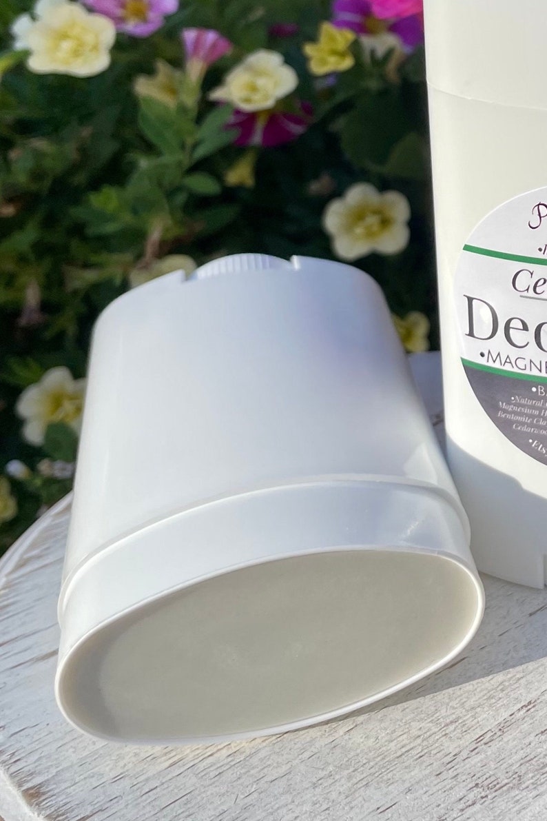 May include: A white deodorant stick with a label that reads 'Cedarwood Deodorant' and 'MAGNESIUM HYDROXIDE'. The deodorant is sitting on a white wooden surface.