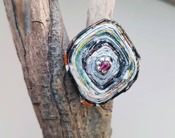 Bague avec un cabochon en papier recyclé et vernis, dans des tons multicolores avec au centre une petite fleur et une perle rose.