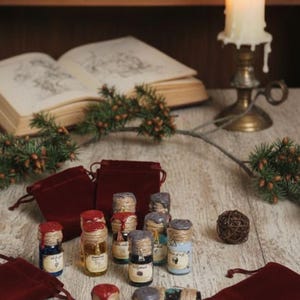 Peut inclure: Une collection de petites bouteilles en verre avec des liquides colorés et des sceaux de cire, disposées sur une surface en bois. Les bouteilles sont accompagnées de petits pochons en velours rouge et d'une bougie allumée dans un bougeoir en laiton. Un livre et une boussole sont en arrière-plan.