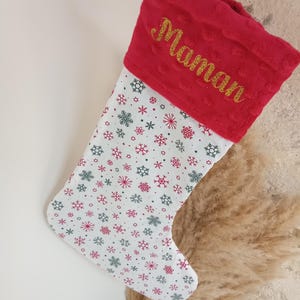 K&ouml;nnte beinhalten: Roter und wei&szlig;er Weihnachtssocken mit Schneeflockenmuster und dem Wort "Maman" in goldenen Glitzer auf dem B&uuml;ndchen gestickt.