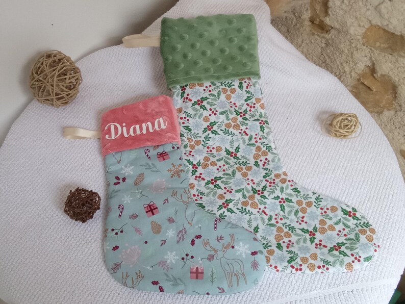 K&ouml;nnte beinhalten: Zwei Weihnachtsstr&uuml;mpfe mit einem gr&uuml;n-wei&szlig;en Blumenmuster. Ein Strumpf hat einen rosa Bund mit dem Namen "Diana" bestickt. Der andere Strumpf hat einen gr&uuml;nen Pl&uuml;schbund.