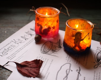 May include: Two glass candle holders with a warm glow. One features a silhouette of a squirrel with stars, the other a silhouette of a person holding a lantern. Both are decorated with colourful paint.