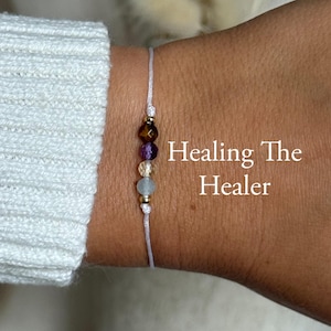 Könnte beinhalten: Ein zartes Armband mit einer Reihe farbiger Edelsteine, darunter Tigerauge, Amethyst, Citrin und Aquamarin. Das Armband wird an einem Handgelenk präsentiert, mit dem Text "Healing The Healer" und den Edelsteinbezeichnungen.
