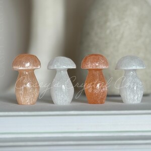 May include: Four crystal mushroom figurines in peach and white hues are displayed on a white surface. The text at the bottom reads, "You will receive 1 mushroom. Your choice of peach colored or white."