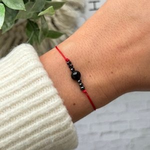May include: A red string bracelet with black beads and a larger black bead in the center.