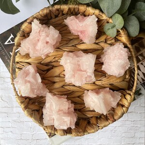 May include: A wicker basket filled with six pink Himalayan salt crystals. The crystals are various sizes and shapes, with a rough, natural texture.