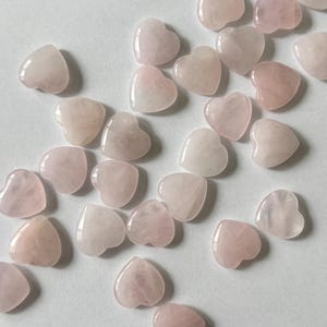 Puede incluir: Una colecci&oacute;n de cristales de cuarzo rosa en forma de coraz&oacute;n rosa. Los cristales son de varios tama&ntilde;os y formas, y todos est&aacute;n pulidos.