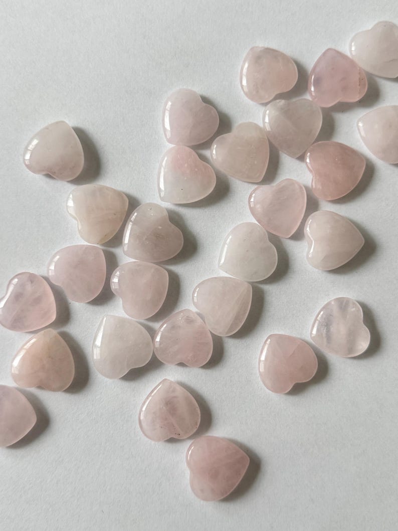 Puede incluir: Una colecci&oacute;n de cristales de cuarzo rosa en forma de coraz&oacute;n rosa. Los cristales son de varios tama&ntilde;os y formas, y todos est&aacute;n pulidos.