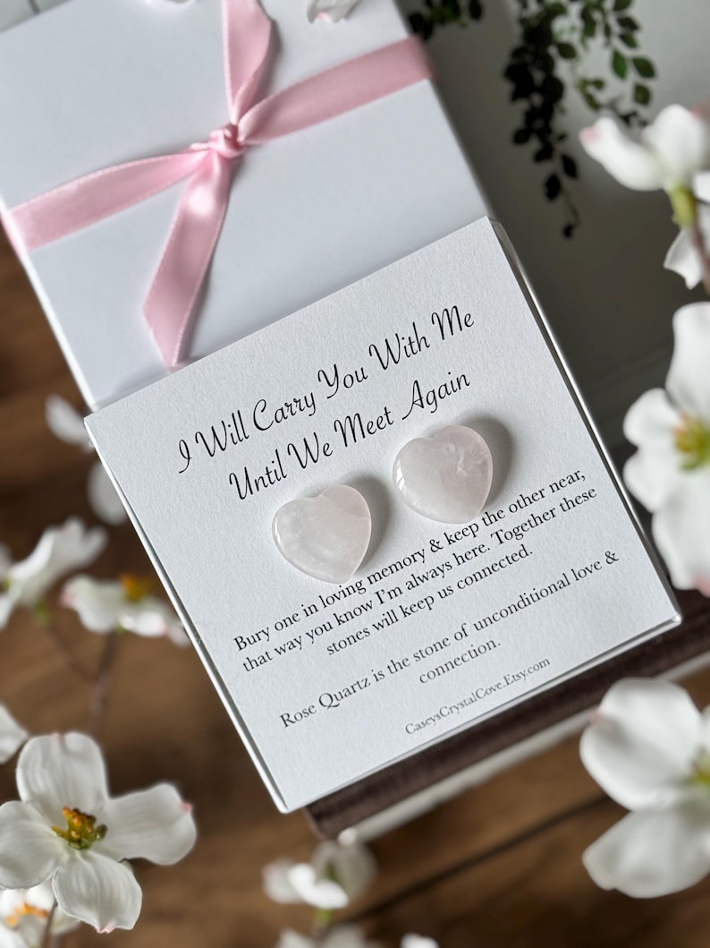 Puede incluir: Una tarjeta blanca con el texto "I Will Carry You With Me Until We Meet Again" y dos piedras en forma de coraz&oacute;n de cuarzo rosa. El texto debajo de las piedras dice "Bury one in loving memory & keep the other near, that way you know I'm always here. Together these stones will keep us connected. Rose Quartz is the stone of unconditional love & connection. CaseysCrystalCove.Etsy.com"