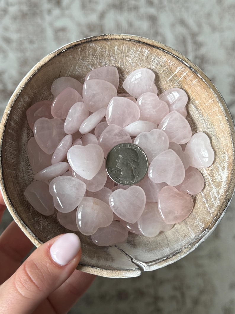 Puede incluir: Un bol lleno de piedras de cuarzo rosa en forma de coraz&oacute;n. El bol est&aacute; hecho de madera clara y tiene un acabado natural. Se incluye una moneda de 25 centavos de d&oacute;lar estadounidense para la escala.