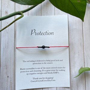 May include: Red string bracelet with black tourmaline beads. The card reads "Protection" and explains the benefits of the stones. "The red string is believed to bring good luck and protection to the wearer. Black tourmaline is one of the most coveted stones for protection and cleansing. It's a great stone for soaking up negative energies and blocks EMF's. Thank you for shopping! CaseysCrystalCove.Etsy.Com"