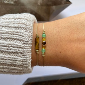 May include: Two bracelets with natural stone beads. One bracelet has a brown tiger's eye stone bar and the other has green and brown beads.