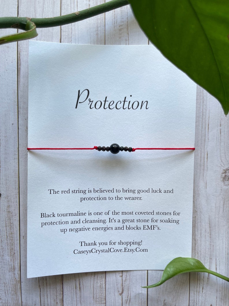 May include: Red string bracelet with a black tourmaline bead. The card reads "Protection" and explains the benefits of the stone. "The red string is believed to bring good luck and protection to the wearer. Black tourmaline is one of the most coveted stones for protection and cleansing. It's a great stone for soaking up negative energies and blocks EMF's. Thank you for shopping! CaseysCrystalCove.Etsy.Com"