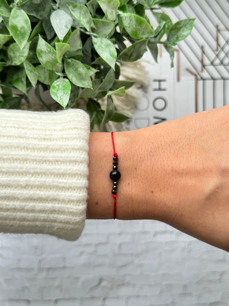 May include: A red string bracelet with a black gemstone bead and silver beads.