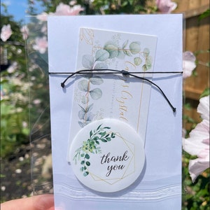 May include: A white card with a thank you sticker on it. The sticker has a gold geometric frame with green leaves and the words "thank you" in the center. The card is in a clear plastic bag.