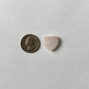 Puede incluir: Un cristal de color rosa p&aacute;lido en forma de coraz&oacute;n junto a una moneda de veinticinco centavos de d&oacute;lar estadounidense para comparar el tama&ntilde;o.