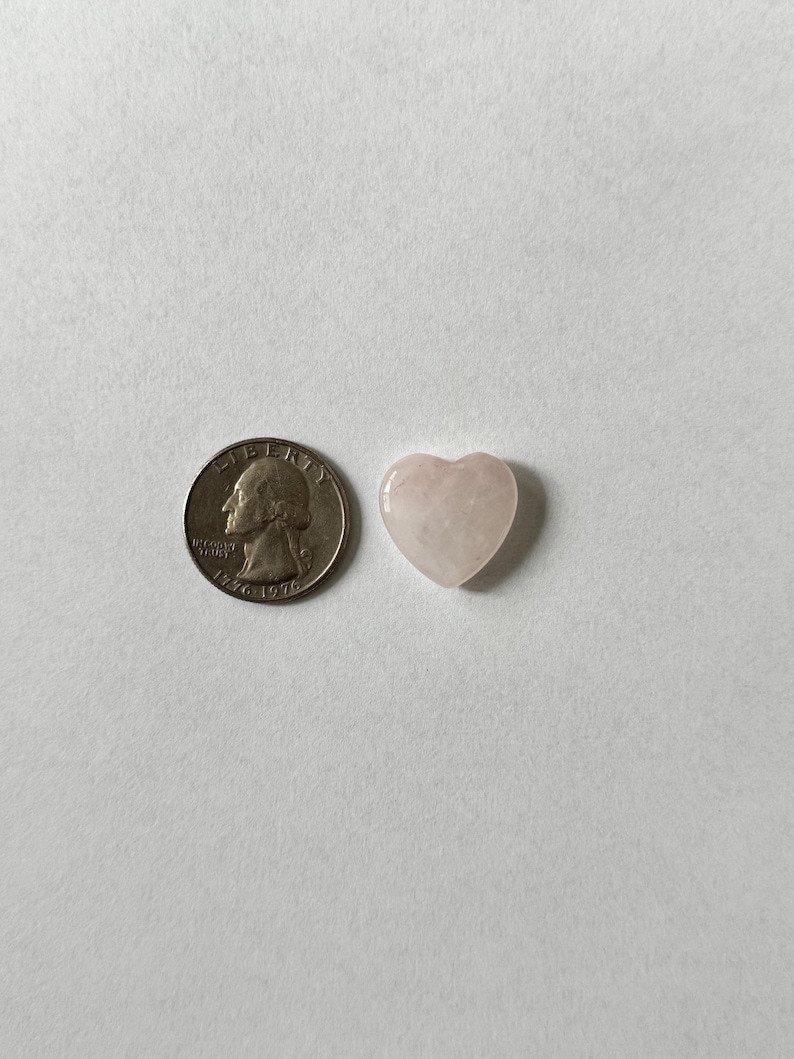 Puede incluir: Un cristal de color rosa p&aacute;lido en forma de coraz&oacute;n junto a una moneda de veinticinco centavos de d&oacute;lar estadounidense para comparar el tama&ntilde;o.
