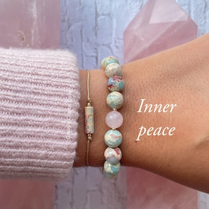 Puede incluir: Dos pulseras, una con cuentas de aqua terra y otra con cuentas de cuarzo rosa. Las pulseras están en la muñeca de una persona. El texto "Inner peace" está escrito en la imagen.