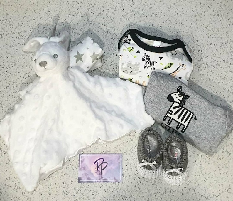 May include: A baby gift set with a white plush animal, a gray and white blanket, a white and gray patterned onesie, and a pair of gray knitted booties.