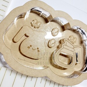 May include: A wooden cloud-shaped tray with a clear epoxy resin insert. The tray features a bunny rabbit, a coffee pot, and coffee beans. The text "Buddie Buddie Designs" is engraved on the tray.