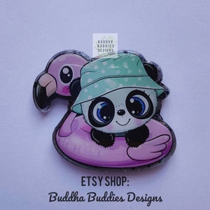 May include: A panda wearing a green and white polka dot hat is riding a pink inflatable flamingo. The panda has big blue eyes and a black nose. The image has a glittery background. ETSY SHOP: Buddha Buddies Designs