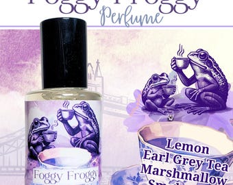 May include: A perfume bottle with a black cap and a label featuring two purple frogs drinking tea. The words "Foggy Froggy Perfume" are at the top. The label also lists the scents: Lemon, Earl Grey Tea, Marshmallow, and Smoky Fog.