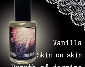 May include: A clear glass bottle with a black cap and label that reads "Lace on Bated Breath". The bottle is sitting on a black surface with a white lace pattern in the background. The text "Vanilla Skin on Skin Breath of Jasmine" is written below the bottle.