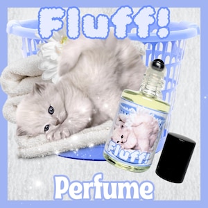 May include: A glass bottle of perfume with a white kitten on the label. The bottle has a black rollerball top and a black cap. The label says "Fluff! Perfume".