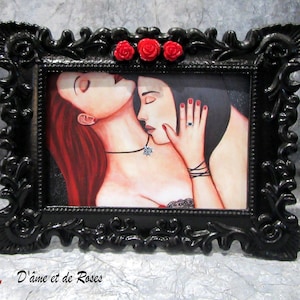 Peut inclure: Une peinture encadrée représentant deux personnes qui s'embrassent. La femme a de longs cheveux roux et l'homme a les cheveux noirs. La femme porte un collier en argent avec un pendentif. L'homme porte un bracelet noir. La peinture est encadrée dans un cadre noir orné avec des roses rouges sur le dessus.