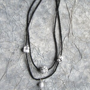 Puede incluir: Un collar de cuentas negro con un colgante. El collar tiene dos hilos y presenta cuentas con dise&ntilde;os en blanco y negro. El colgante es un dise&ntilde;o de tablero de ajedrez en blanco y negro con una rosa roja en el centro. Una joya &uacute;nica.