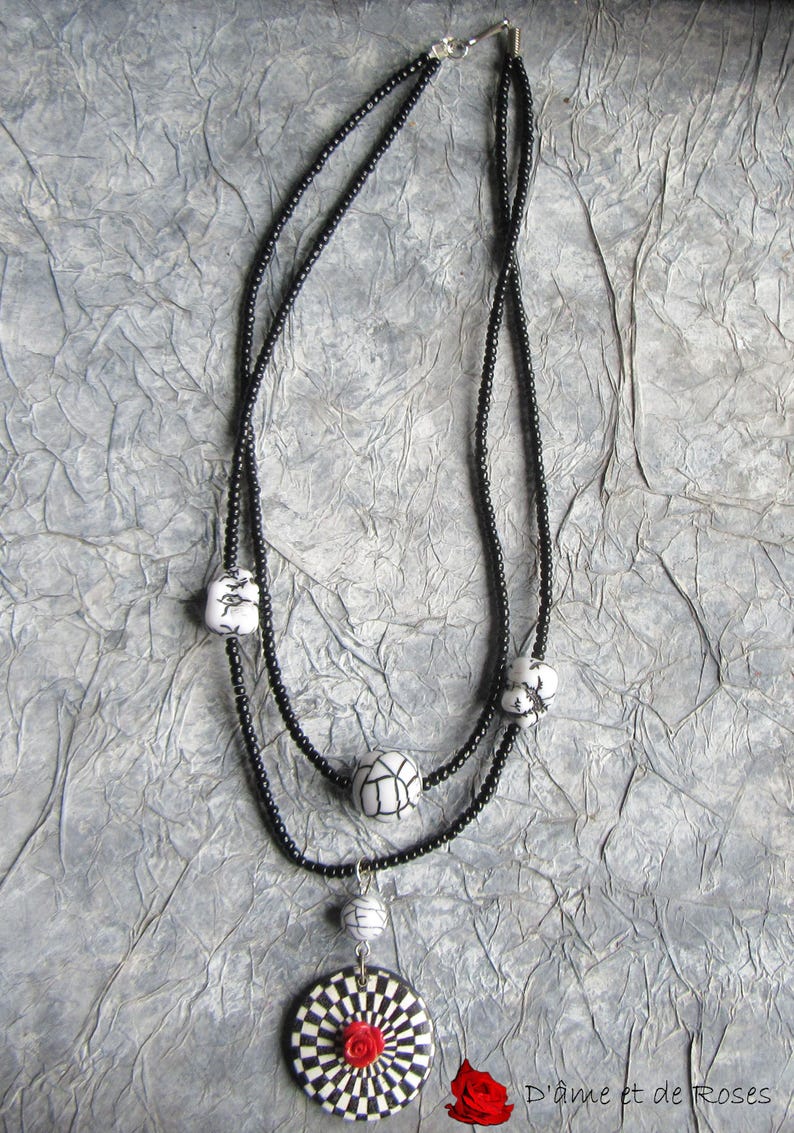 Puede incluir: Un collar de cuentas negro con un colgante. El collar tiene dos hilos y presenta cuentas con dise&ntilde;os en blanco y negro. El colgante es un dise&ntilde;o de tablero de ajedrez en blanco y negro con una rosa roja en el centro. Una joya &uacute;nica.