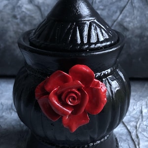 Peut inclure: Pot en céramique noire avec un couvercle et un accent de rose rouge. Le pot a un design décoratif et une base large.