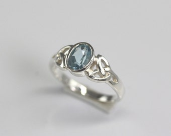 Könnte beinhalten: Ein silberner Ring mit einem blauen Edelstein, der in einem keltischen Knotendesign eingefasst ist.