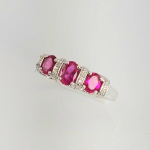 May include: A silver ring with four oval-shaped pink gemstones and smaller clear gemstones set in a band.