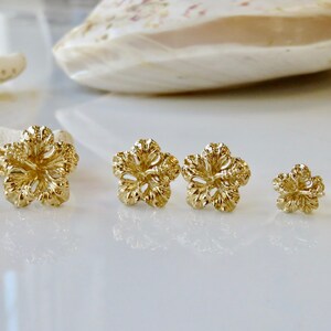 May include: A set of six gold-tone flower-shaped stud earrings. The earrings are arranged in order of size, with the largest earrings on the left and the smallest earrings on the right.