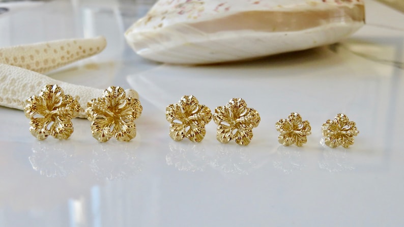 May include: A set of six gold-tone flower-shaped stud earrings. The earrings are arranged in order of size, with the largest earrings on the left and the smallest earrings on the right.