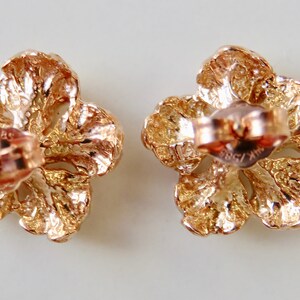 May include: A pair of gold-tone flower-shaped earrings with a textured finish. The earrings have a post and butterfly closure.
