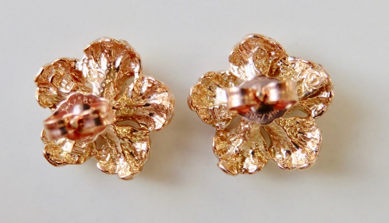 May include: A pair of gold-tone flower-shaped earrings with a textured finish. The earrings have a post and butterfly closure.
