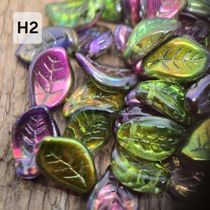 May include: A selection of iridescent leaf-shaped beads in green, purple, and gold. Each bead features a detailed leaf vein pattern. The image includes the text "H2" in a white box.