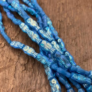 Puede incluir: Una hebra de cuentas de vidrio azul iridiscente con un diseño de búho. Las cuentas están enhebradas en un hilo transparente y tienen aproximadamente 1,2 cm de largo.