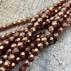 May include: A strand of faceted glass beads in a rich copper color. The beads are round and have a metallic sheen.