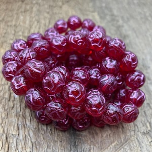 May include: A strand of deep pink glass beads with a rose design. The beads are round and have a glossy finish.
