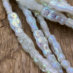 May include: A strand of iridescent white glass beads with an owl design. The beads are strung together and have a pearlescent finish.