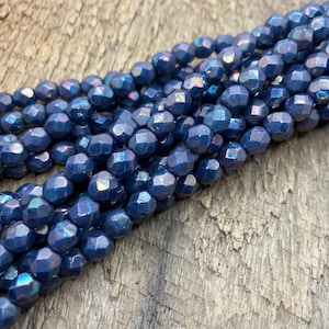 May include: A strand of dark blue faceted glass beads with iridescent shimmer. The beads are round and have a slightly irregular shape.