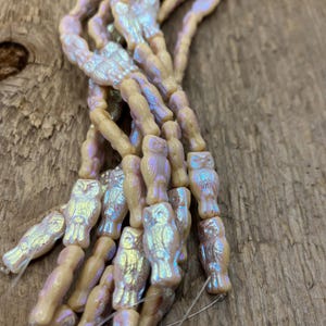 Puede incluir: Una hebra de cuentas de vidrio iridiscente con diseños de búhos. Las cuentas son de color crema pálido con un acabado nacarado.