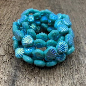 May include: A strand of turquoise blue glass beads with a shell-like texture. The beads are iridescent and have a slightly pearlescent finish.
