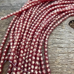 May include: A strand of red faceted glass beads with a metallic sheen. The beads are small and round, and they are strung together on a clear thread.