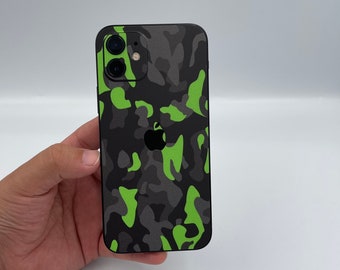 May include: A smartphone featuring a black, gray, and bright lime green camouflage pattern skin applied to the back. The device includes a dual-lens camera module in the upper left corner and a centered Apple logo visible through the camouflage skin.